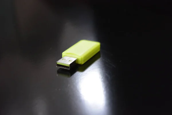 Bright light green computer USB flash drive for the accumulation and storage of information located on a black glossy surface.