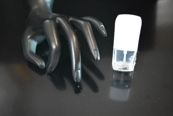A black matte ceramic hand-made statuette with female transparent nail polish is located on a black matte background.