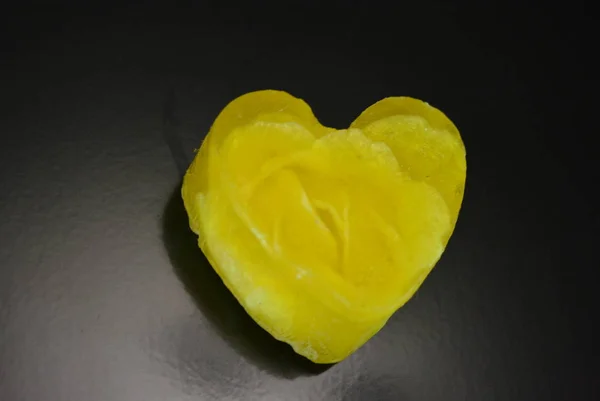 A delicate yellow smelling handmade soap with flowers and rose petals inside in the form of love and heart lies on a black glossy surface with reflection.