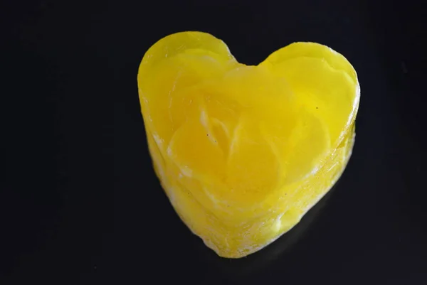 A delicate yellow smelling handmade soap with flowers and rose petals inside in the form of love and heart lies on a black glossy surface with reflection.