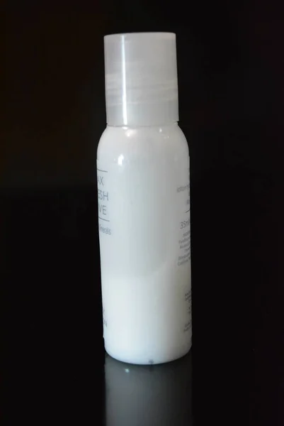 A white small plastic bottle with cosmetic and medical products for body and beauty care is on a glossy black surface.