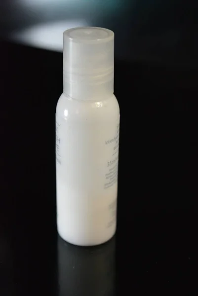 A white small plastic bottle with cosmetic and medical products for body and beauty care is on a glossy black surface.