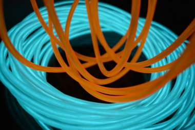 Siyah parlak bir yüzey üzerinde bulunan turuncu Bir ışık kılavuzu kaotik teller ile turkuaz, gökyüzü mavisi parlak tel parlak bir bobin. Işık tuval, teller ve sanat arka plan ile arka aydınlatma.