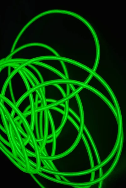 Toxic green luminous electroluminescence wires with different shapes and structures. A web of lime electroluminescent fiber, el wires and unusual circles located on a black glossy surface.