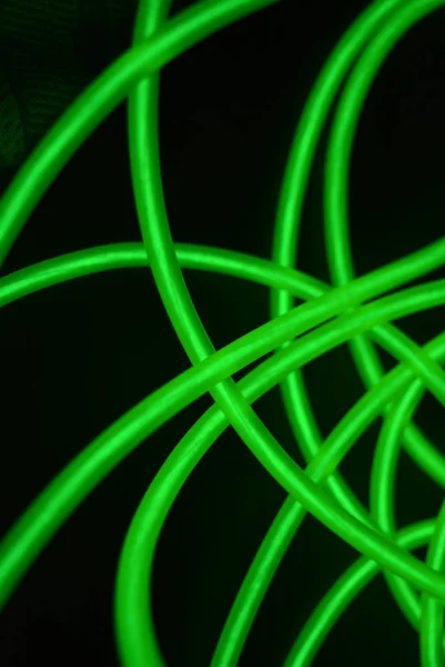 Toxic green luminous electroluminescence wires with different shapes and structures. A web of lime electroluminescent fiber, el wires and unusual circles located on a black glossy surface.