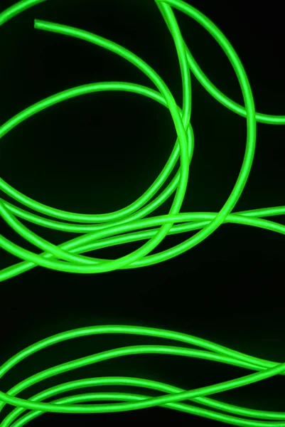 Toxic green luminous electroluminescence wires with different shapes and structures. A web of lime electroluminescent fiber, el wires and unusual circles located on a black glossy surface.