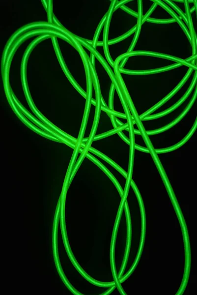 Toxic green luminous electroluminescence wires with different shapes and structures. A web of lime electroluminescent fiber, el wires and unusual circles located on a black glossy surface.