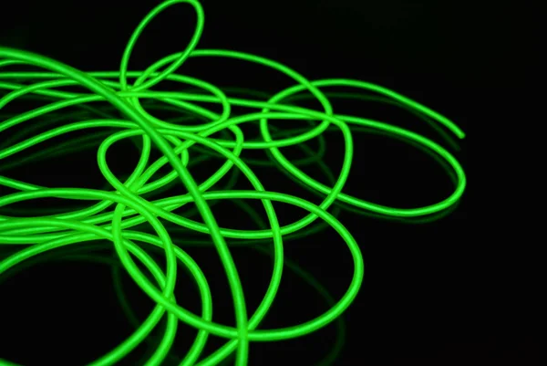 Toxic green luminous electroluminescence wires with different shapes and structures. A web of lime electroluminescent fiber, el wires and unusual circles located on a black glossy surface.