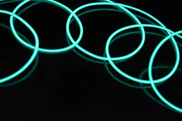 Unusual bright wires made of turquoise-colored material glowing at night. Chaotic sky blue wires, light guide electroluminescent wires, electroluminescence are located on a glossy black surface.