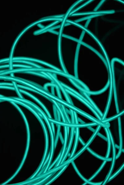 Unusual bright wires made of turquoise-colored material glowing at night. Chaotic sky blue wires, light guide electroluminescent wires, electroluminescence are located on a glossy black surface.