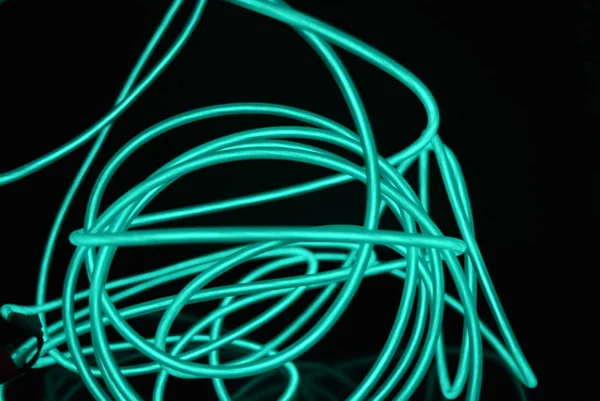 Unusual bright wires made of turquoise-colored material glowing at night. Chaotic sky blue wires, light guide electroluminescent wires, electroluminescence are located on a glossy black surface.