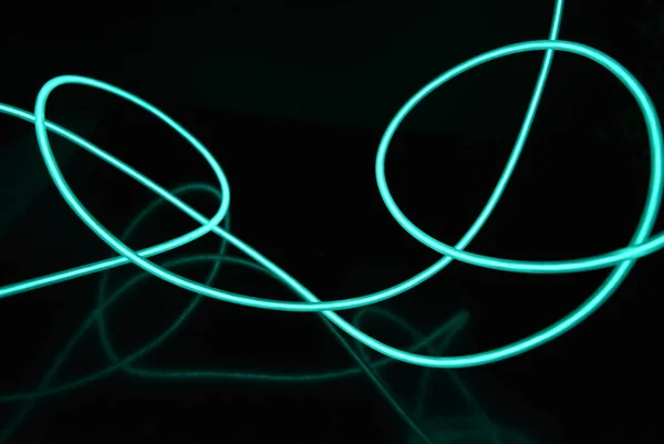 Unusual bright wires made of turquoise-colored material glowing at night. Chaotic sky blue wires, light guide electroluminescent wires, electroluminescence are located on a glossy black surface.