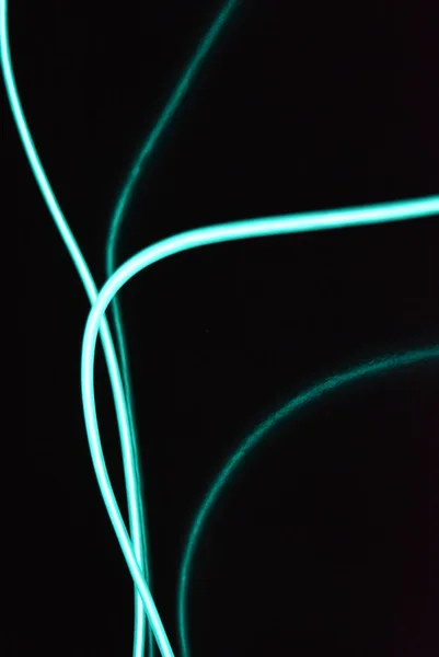 Unusual bright wires made of turquoise-colored material glowing at night. Chaotic sky blue wires, light guide electroluminescent wires, electroluminescence are located on a glossy black surface.