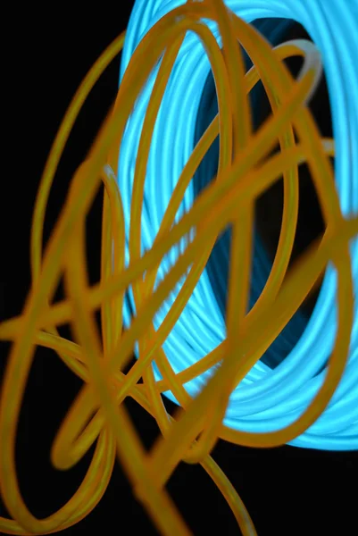 A bright coil of turquoise, sky blue luminous wire with chaotic wires of an orange light guide located on a black glossy surface. Light canvas, backlighting with wires and art background.