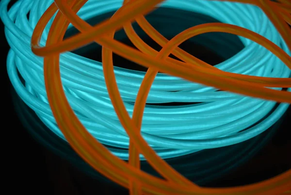 A bright coil of turquoise, sky blue luminous wire with chaotic wires of an orange light guide located on a black glossy surface. Light canvas, backlighting with wires and art background.