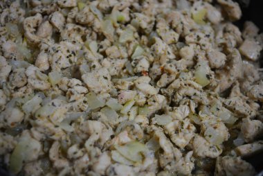 İnce doğranmış ev yapımı tavuk göğsü, kızartılmış ve soğan ve ayçiçeği yağı ile pişirilmiş. Lezzetli, sulu tavuk dilimleri kızarırken siyah bir tavanın üzerinde yatıyor..