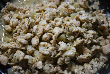 İnce doğranmış ev yapımı tavuk göğsü, kızartılmış ve soğan ve ayçiçeği yağı ile pişirilmiş. Lezzetli, sulu tavuk dilimleri kızarırken siyah bir tavanın üzerinde yatıyor..