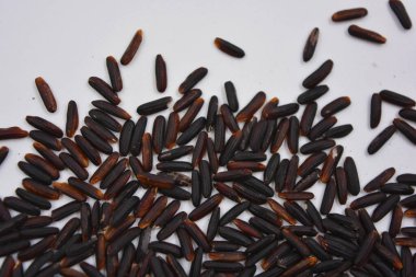 Beyaz bir tabağa serpiştirilmiş, uzun, cilalanmamış, kullanışlı siyah pirinç. Sağlıklı yiyecekler, sağlıklı mısır gevrekleri. Her gün için doğal pirinç..