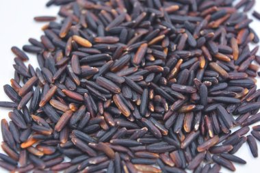 Beyaz bir tabağa serpiştirilmiş, uzun, cilalanmamış, kullanışlı siyah pirinç. Sağlıklı yiyecekler, sağlıklı mısır gevrekleri. Her gün için doğal pirinç..