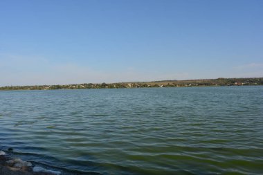 Güzel, parlak doğa, Ukrayna, Samara Nehri yakınlarındaki manzara. Ağaçları ve güzel yeni evleri olan yeşil bir bankanın arka planında küçük dalgalarla dolu derin mavi bir nehir..