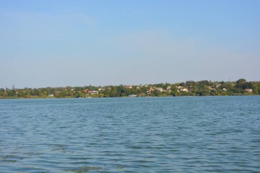 Güzel, parlak doğa, Ukrayna, Samara Nehri yakınlarındaki manzara. Ağaçları ve güzel yeni evleri olan yeşil bir bankanın arka planında küçük dalgalarla dolu derin mavi bir nehir..
