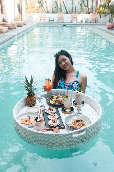 Pretty Asian woman eating breakfast in the pool, floating breakf