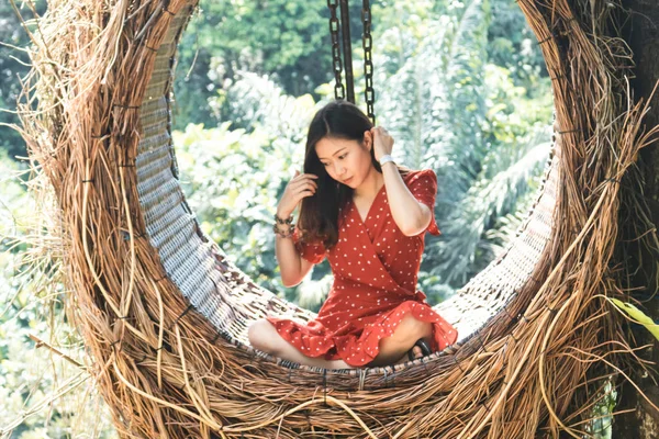 Pretty Asian woman is sitting on straw nest, Ubud, Bali.