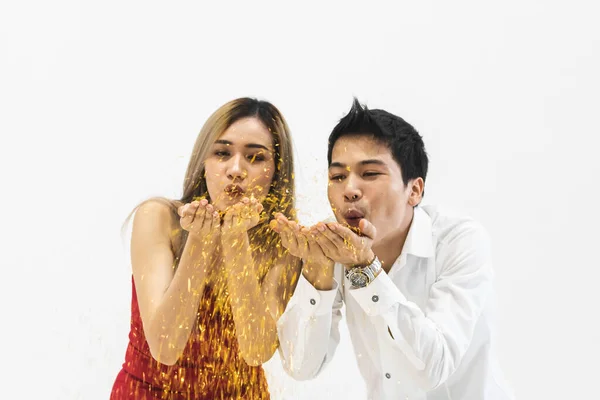close up of young Asian couple blowing confetti together with white background.