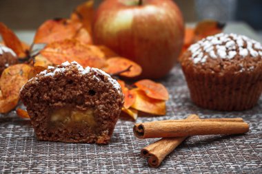 Sonbahar yaprakları ve elmaların arka planında lezzetli elma dolgulu çikolatalı kekler ve krema şekeri.