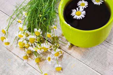 Ahşap bir arka planda yeşil fincanda siyah çay ve papatya çayı.