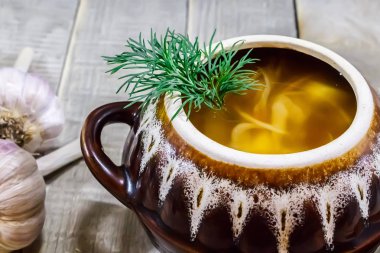 Bir tencerede sebze çorbası, ekmek ve gri ahşap arka planda taze sarımsak.