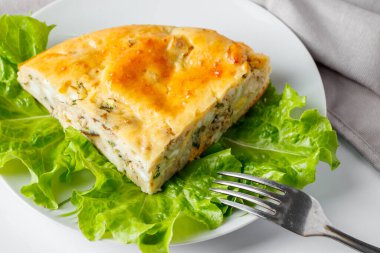 Tabakta lezzetli balık turtası. Beyaz arka planda uskumru ve yeşillikler olan bir dilim pasta..