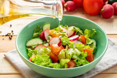 Ahşap arka planda seramik kasede zeytinyağlı taze sebze salatası. Mevsimlik domates, salatalık ve turp tabağı..