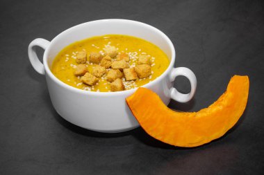 Krakerli balkabağı kremalı çorba. Kraker ve susam tohumlu balkabağı kremalı çorba. Arka planda beyaz bir bulyon.