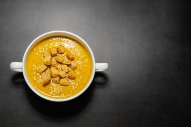 Krakerli balkabağı kremalı çorba. Koyu arkaplanda beyaz bir bulyon içinde beyaz krakerli balkabağı kremalı çorba.