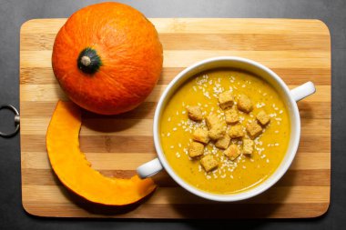 Ahşap zemin üzerinde susam tohumları olan sonbahar balkabağı çorbası. Balkabağı çorbası ve ahşap arka planda bir dilim sonbahar sebzesi.