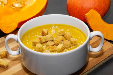 Ahşap zemin üzerinde susam tohumları olan sonbahar balkabağı çorbası. Yakın plan balkabağı çorbası yakın çekim ve kaşık