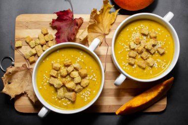 Ahşap zemin üzerinde susam tohumları olan sonbahar balkabağı çorbası. İki kâse balkabağı çorbası ve kahverengi arka planda sonbahar yaprakları.