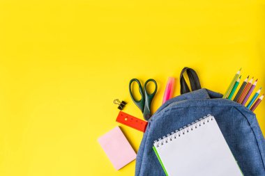 Sırt çantası ve ofis malzemeleri sarı arka planda yatıyordu. Okul konseptine geri dönelim. Metin için yer.