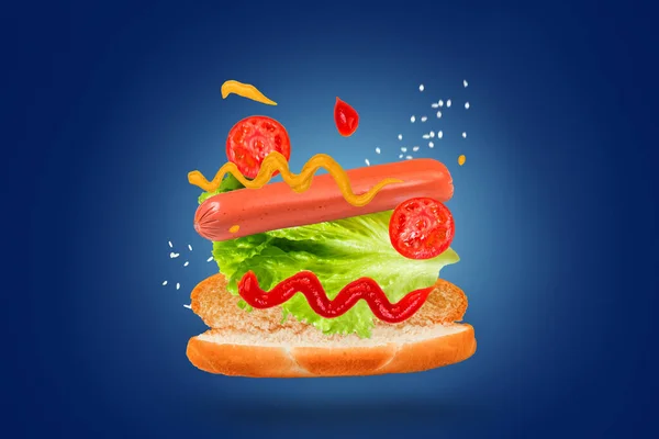 Delicious hot dog with flying ingredients on a blue background. Levitating food.