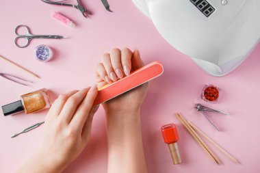 Kadın evde manikür yapıyor. Pembe arka planda tırnak törpüsü olan eller.