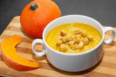 Ahşap zemin üzerinde susam tohumları olan sonbahar balkabağı çorbası. Kahverengi ahşap zemin üzerinde uygun beslenme için balkabağı çorbası