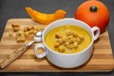 Ahşap zemin üzerinde susam tohumları olan sonbahar balkabağı çorbası. Tabakta çorba ve tahta arka planda balkabağı dilimleri.