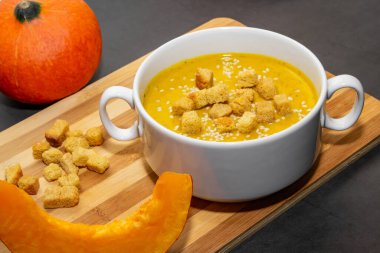 Ahşap zemin üzerinde susam tohumları olan sonbahar balkabağı çorbası. Sonbahar balkabağı çorbası ve kaşığı. Vejetaryen yemeği.