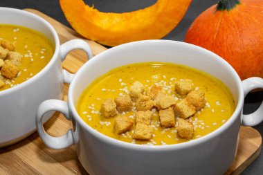 Ahşap zemin üzerinde susam tohumları olan sonbahar balkabağı çorbası. Portakallı vejetaryen balkabağı çorbası ve kraker.