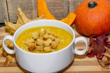 Ahşap zemin üzerinde susam tohumları olan sonbahar balkabağı çorbası. Sonbahar yapraklarının arka planında kraker ve susam tohumlu kabak püresi çorbası.