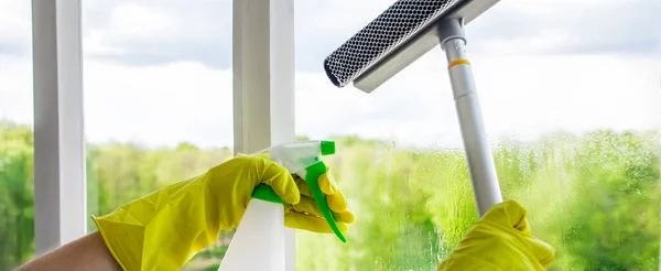 Washing windows. Home cleaning concept. Woman in yellow rubber gloves spray liquid for glasses. Banner format.