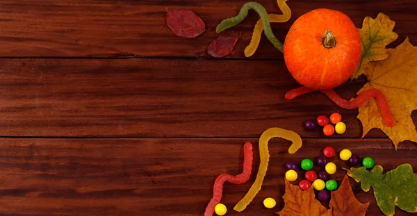Traditional Halloween sweets. Pumpkins, autumn leaves and candies on a wooden background. Banner format
