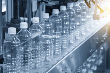 İçme suyu fabrikasındaki işlemleri tamamlamak için konveyör bandındaki PET şişeleri. Plastik şişe üretim sürecinin yüksek teknolojisi..