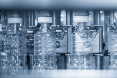 Mavi ton sahnesindeki otomatik içme suyu şişesi doldurma işlemi. Taşıma bandındaki içme suyunun seri üretimi. 